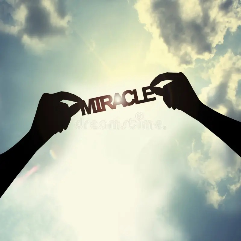 Two hands holding the word "miracle" looking up towards the sky sunlight and clouds in the background
