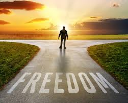 A person stands at a T junction, just in front of the word 'Freedom' written on the road